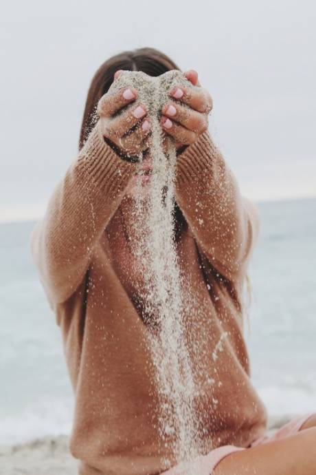 Девушка у моря сыплет песок сквозь пальцы