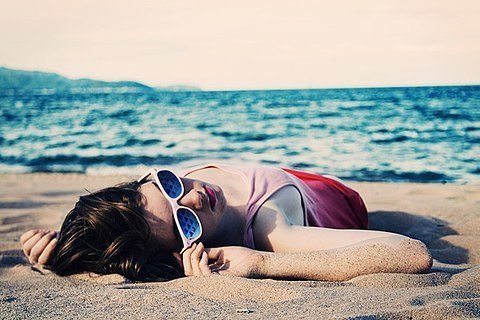 девушка в солнечных очках лежит на пляже
