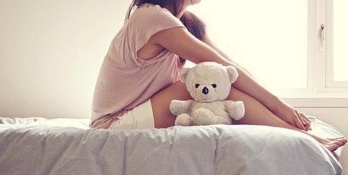 Девушка с плюшевым мишкой сидит на кровати