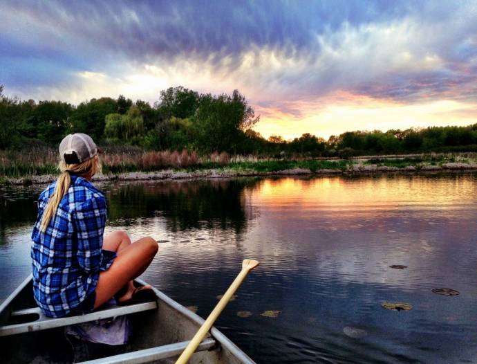 Девушка в клетчатой рубашке в лодке глядит на реку