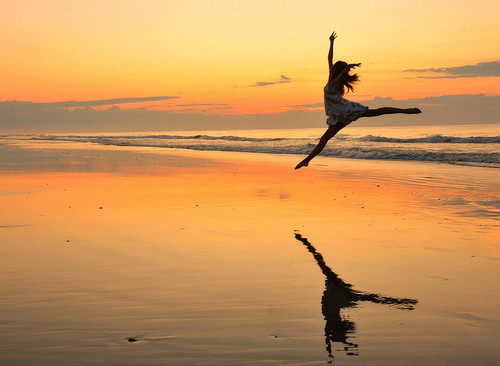 Девушка в прыжке над берегом моря на закате