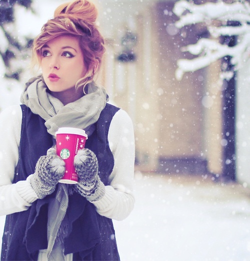 Девушка в варежках под снегом держит стакан кофе