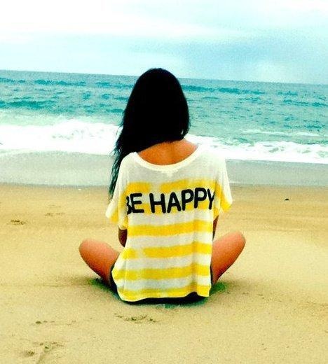 Надпись Be Happy на майке девушки, сидящей у моря