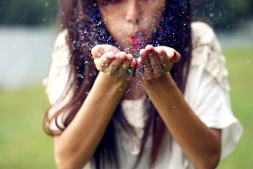 Девушка сдувает цветную пыль с ладоней