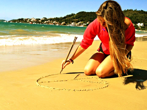 Девушка рисует на песке пляжа знак PEACE