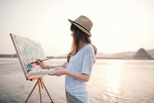 Девушка в шляпе рисует пейзаж у реки на мольберте
