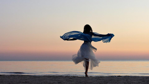 Танцующая у моря девушка в белом платье
