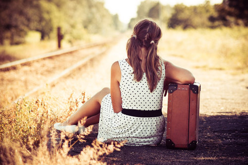 Девушка с чемоданом сидит у железнодорожных путей