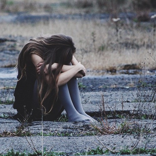 Одинокая девушка, закрыв лицо плачет сидя на земле
