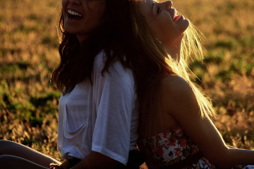 Две смеющиеся девушки сидят на летнем лугу