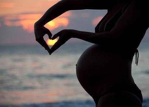 силуэт беременной женщины и солнце в руках