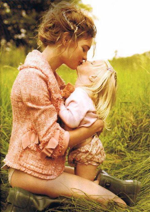 Молодая мама целует свою доченьку на лугу