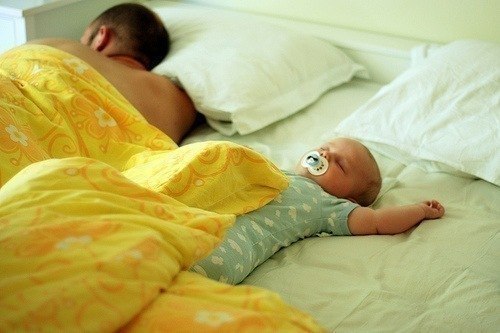 малыш с соской спят на кровати с папой