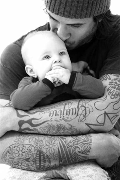 Папа с татуировками на руках целует малыша
