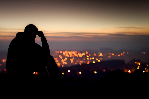 Силуэт парня сидящего на фоне ночных огней города