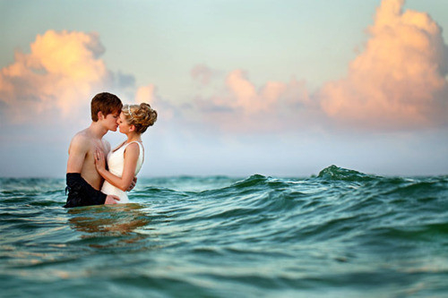 Парень с девушкой стоят в море и целуются