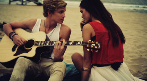 Парень на пляже играет для девушки на гитаре