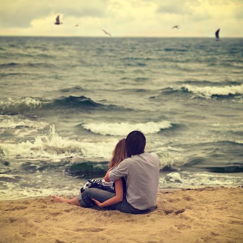 Парень и девушка обнявшись смотрят на волны моря