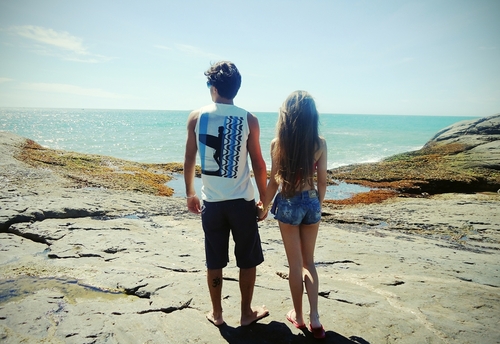 Парень с девушкой взявшись за руки смотрят на море