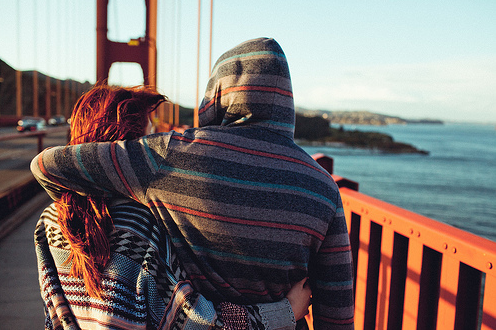 Парень с девушкой в обнимку идут по мосту
