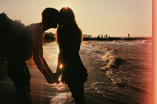 Парень целует девушку у моря на закате