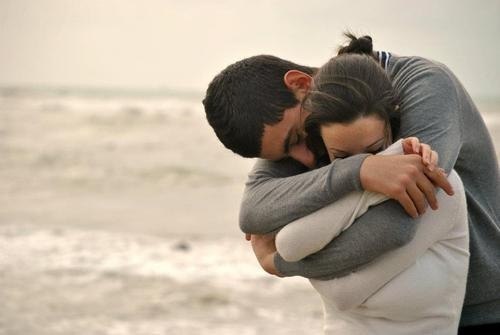 парень обнимает девушку сзади на побережье моря