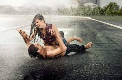 Парень и девушка смеются под дождем на дороге