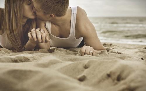 Взявшись за руки,парень и девушка целуются на пляж